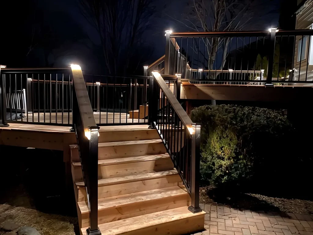 Night view of custom-built wooden deck with black metal railings and built-in LED post cap lighting on stairs